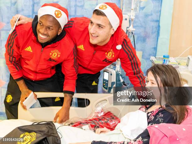 Diogo Dalot and Fred of Manchester United pose with Olivia during the club's annual Christmas hospital visits at Royal Manchester Children's Hospital...