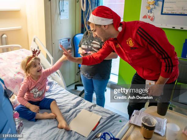 Diogo Dalot and Fred of Manchester United pose with Ellie-Mae during the club's annual Christmas hospital visits at Royal Manchester Children's...