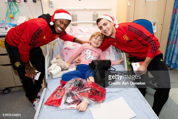 Diogo Dalot and Fred of Manchester United pose with Ellie-Mae during the club's annual Christmas hospital visits at Royal Manchester Children's...