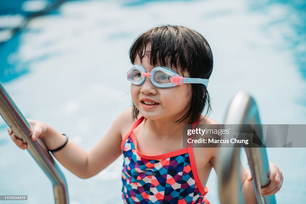 Asian chinese young girl practicing swimming with wearing goggles at her own house swimming pool