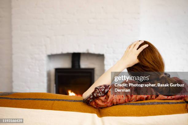 rear view of a woman sitting in front of the fire place, holding her head - autumn sadness stock pictures, royalty-free photos & images