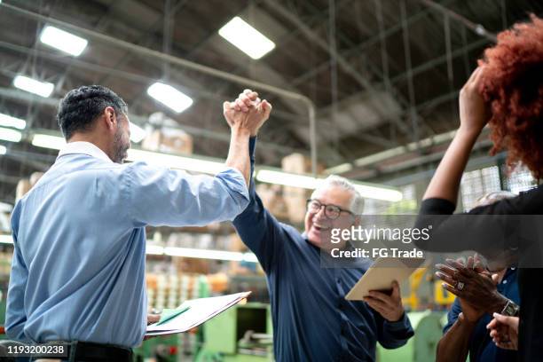 medewerkers vieren goed nieuws in een fabriek - positieve emotie stockfoto's en -beelden