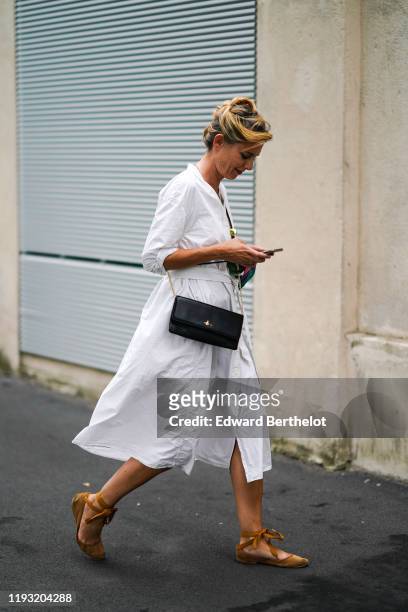 Guest wears a white long sleeves shirt-dress, a black bag, camel suede flat shoes, outside the Prada show during Milan Fashion Week Spring/Summer...