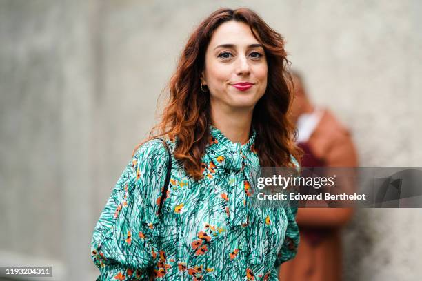 Guest wears earrings, a green top with orange flowers print, puff sleeves and a lavaliere, outside the Prada show during Milan Fashion Week...