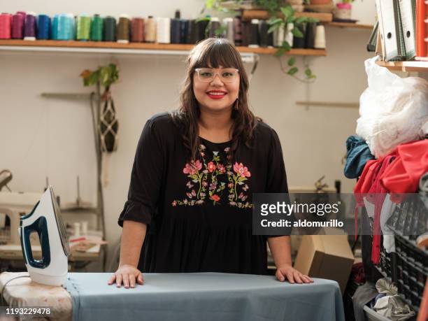 young woman ironing fabric and smiling at camera - mexican business women stock pictures, royalty-free photos & images
