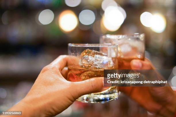two men clinking glasses of whiskey drink alcohol beverage together at counter in the pub - drink stock pictures, royalty-free photos & images