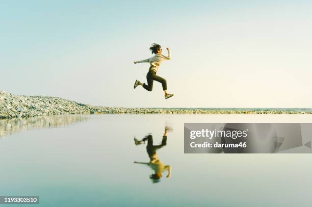 vrouw in mid-air springen boven water weerspiegeld in grote plas. - dream big stockfoto's en -beelden