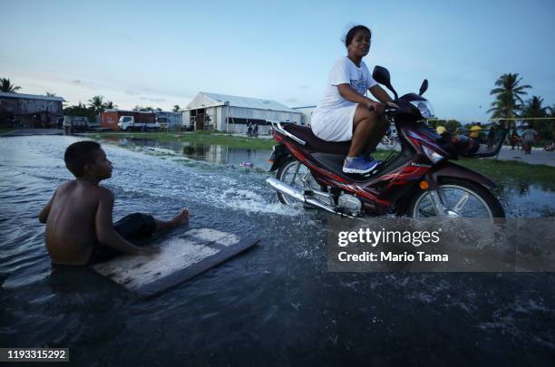 Woman rides her scooter through floodwaters occurring around high tide in a low lying area near the airport on November 27, 2019 in Funafuti, Tuvalu....
