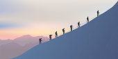 Roped climbers climb the side of a mountain as they walk along a ridge at sunset.