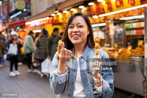 woman eating street food at market - korea market stock pictures, royalty-free photos & images