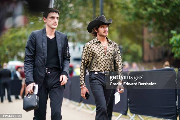 Guest wears a cow boy hat, a shirt with printed golden coins, a belt, black pants, during London Fashion Week September 2019 on September 16, 2019 in...