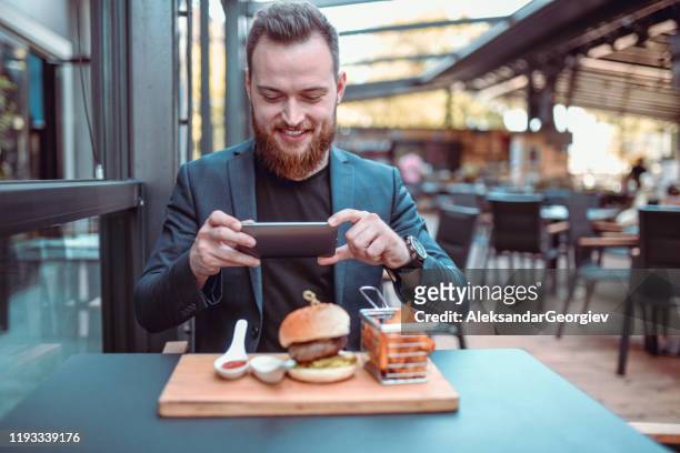 sonriendo elegante macho fotografiando hermosa hamburguesa - male burger eating fotografías e imágenes de stock