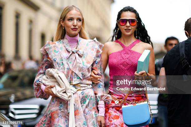 Leonie Hanne wears earrings, a pink turtleneck, a long sleeves, ruffled, light pink dress with colorful flowers print and a lavaliere, a white belt...