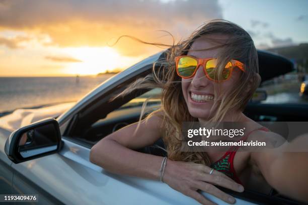 woman on road trip enjoying vacations and nature arms outstretched in convertible vehicle looking at sea - car sunset arm stock pictures, royalty-free photos & images