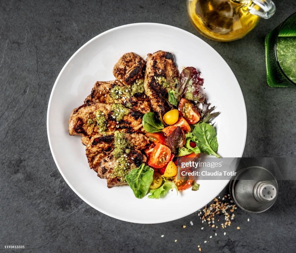 Grilled pork cutlets with salad in a bowl on black background