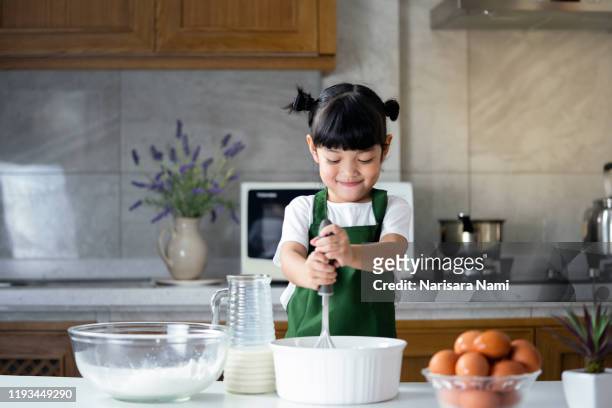 child girl enjoy cooking in the kitchen. happy asian kid is preparing the dough, bake cookies in the kitchen. - kids fun indonesia stock-fotos und bilder