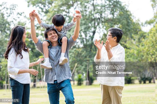 multi asian family spending time in weekend holiday. young father carry kid piggyback in public park happy together. - boy thailand stock pictures, royalty-free photos & images