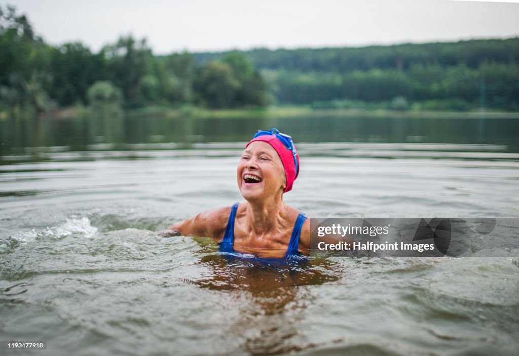 Active senior woman standing in lake outdoors in nature, laughing.