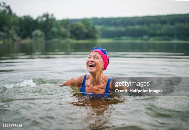active senior woman standing in lake outdoors in nature, laughing. - anziani attivi foto e immagini stock