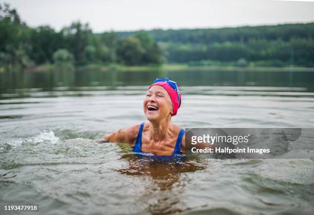 active senior woman standing in lake outdoors in nature, laughing. - swimming stock pictures, royalty-free photos & images