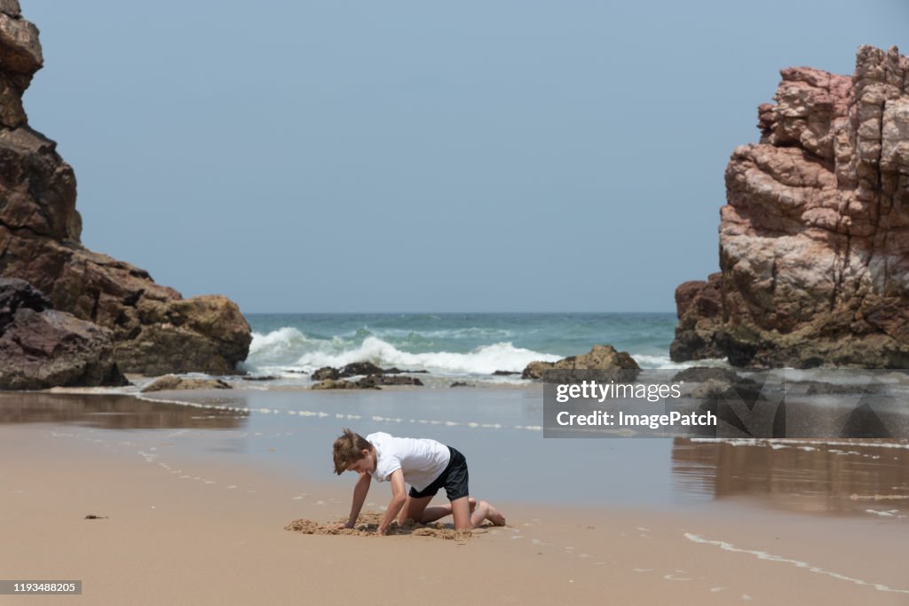 Boy quietly digging in the sand at the beach