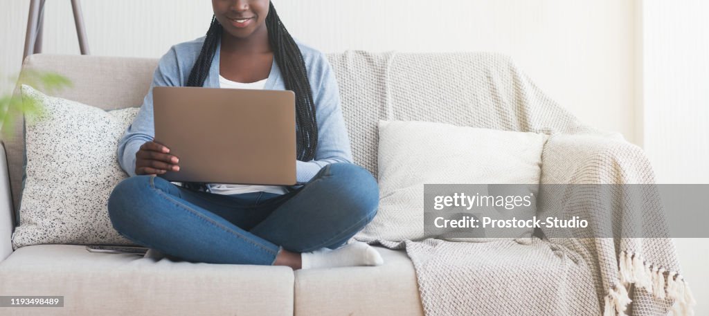 Unrecognizable afro girl using laptop while sitting on sofa at home