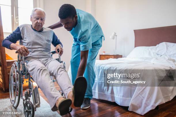 man nurse helping senior in wheelchair in nursing home - paralysis stock pictures, royalty-free photos & images