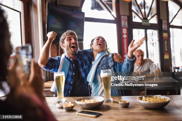 jong stel kijken naar een voetbalwedstrijd in een lokale pub - argentina supporters stockfoto's en -beelden