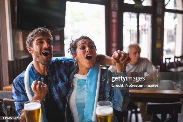 young couple watching a soccer match in a local pub - argentina supporters stock pictures, royalty-free photos & images