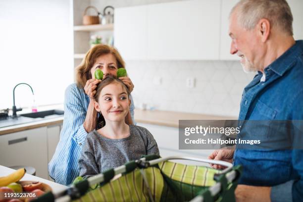senior grandparents and granddaughter unpacking shopping indoors in kitchen, having fun. - granny flat stock pictures, royalty-free photos & images