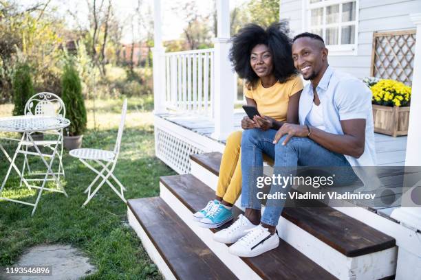 african couple sitting on stairs and looking at smart phone - letting it all hang out stock pictures, royalty-free photos & images