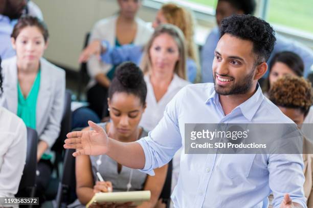 young businessman addresses colleagues during seminar - diverse town hall meeting stock pictures, royalty-free photos & images