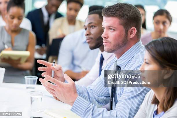 mid adult businessman asks question during meeting - town hall meeting stock pictures, royalty-free photos & images