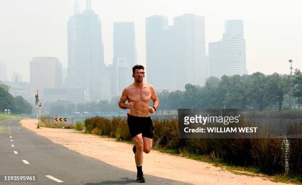 Runner jogs as smoke haze from unprecendented bushfires hover over the city skyline ahead of the Australian Open in Melbourne on January 14, 2020. -...