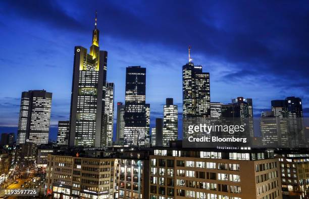 The Commerzbank AG headquarters, second left, and the Deutsche Bank AG twin towers, right, stand illuminated with other skyscrapers in the financial...