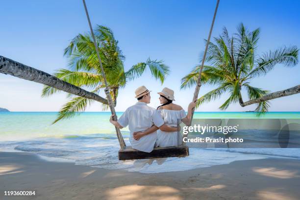 asian couple lover in white dress enjoy honeymoon and long vacation on the sea beach, sitting on the swing together relax and confortable, valentine. summer, travel, vacation and holiday concept. - valentines day couple stock pictures, royalty-free photos & images