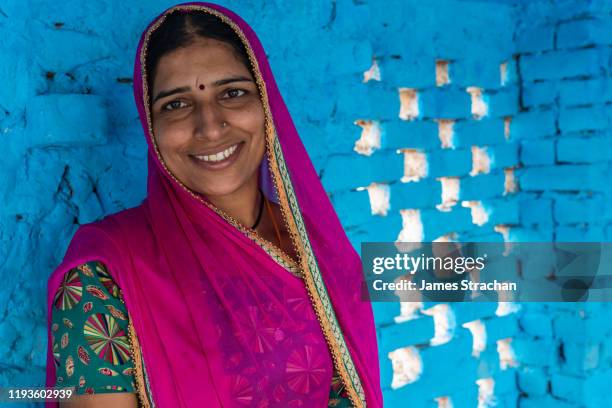 head and shoulders (smiling) portrait of one mid adult female gujar villager in bright pink traditional clothing against blue wall background, pushkar, rajasthan, india (model release) - rajasthani women stock pictures, royalty-free photos & images