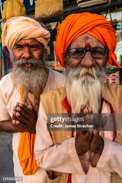 close up portrait of two senior male pilgrims, with turbans and bushy beards, saying namaste, the customary hindu greeting usually spoken with a slight bow and hands pressed together, palms touching and fingers pointing upwards, thumbs close to the chest, - pilgrims and indians stockfoto's en -beelden