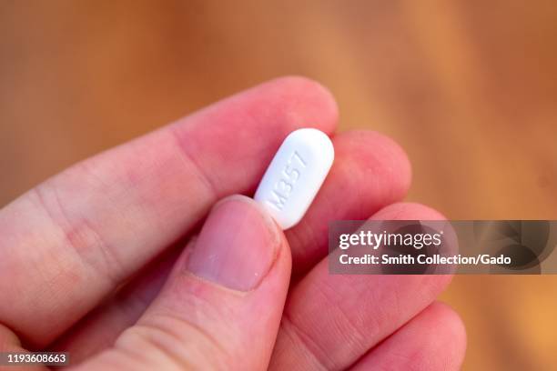 Illustrative image, close-up of hand of a man against a light wooden background holding several pills of the combination narcotic opioid pain...