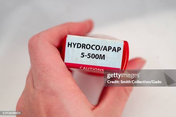 Illustrative image, close-up of hand of a man against a white background holding a bottle of the combination narcotic opioid pain medication...