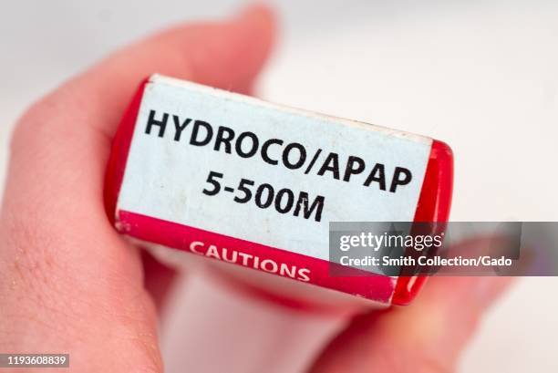 Illustrative image, close-up of hand of a man against a white background holding a bottle of the combination narcotic opioid pain medication...