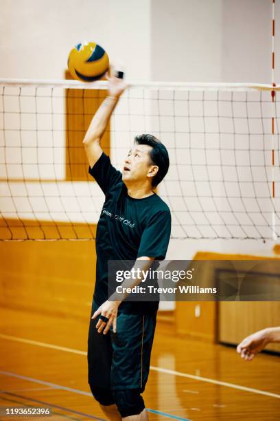 mature man practicing for a community volleyball team - hallenvolleyball stock-fotos und bilder