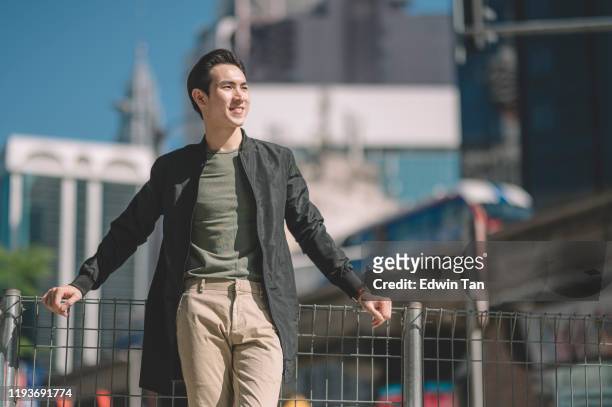 ein asiatischer chinese, der tagsüber mit lässiger kleidung und jacke am zaun des fußgängerweges in der stadt lehnt - asain model men stock-fotos und bilder