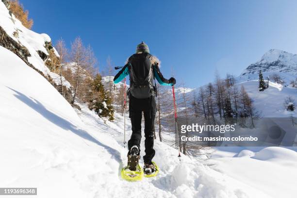 woman walking with snowshoes on snowy mountain path - schneeschuh stock-fotos und bilder