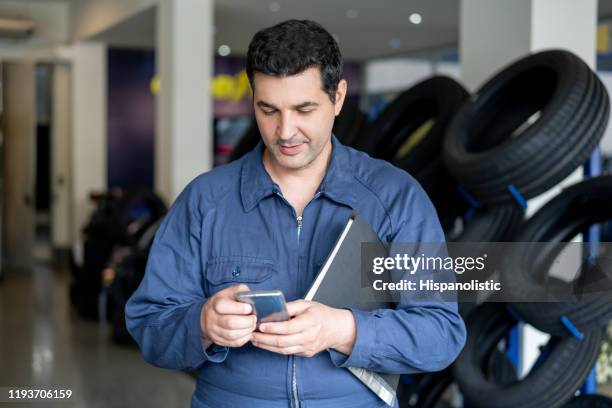 cheerful mechanic taking a break at the car workshop texting on smartphone - repairman phone stock pictures, royalty-free photos & images