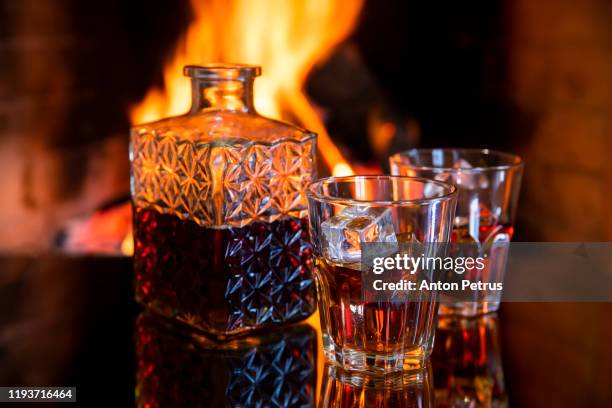 two glasses and a of whiskey near the fireplace. - cognac fotografías e imágenes de stock