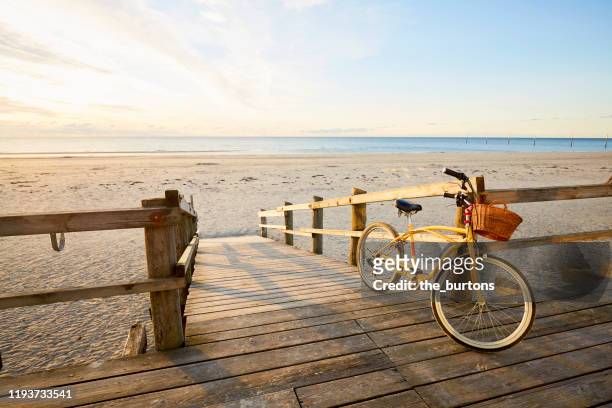 yellow beachcruiser bicycle leaning at a railing at an empty beach during sunrise - boardwalk ストックフォトと画像