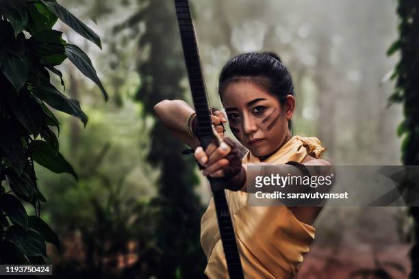 beautiful archer is aiming her longbow to shoot in jungle with beautiful sunlight background - hunting longbow - fotografias e filmes do acervo