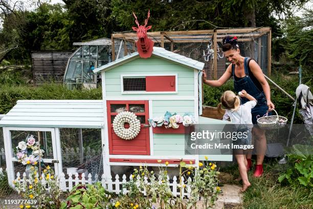 smiling woman and girl standing in a garden next to a colourful hen house. - kippenhok stockfoto's en -beelden
