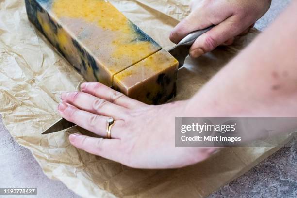 high angle close up person cutting yellow and black homemade bar of soap with kitchen knife. - homemade soap stock pictures, royalty-free photos & images